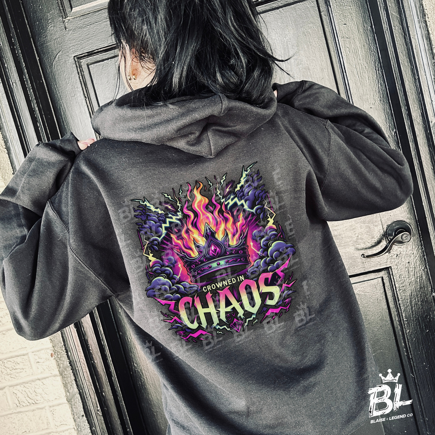 Unisex black hoodie with 'Crowned in Chaos' text and edgy neon flame artwork.